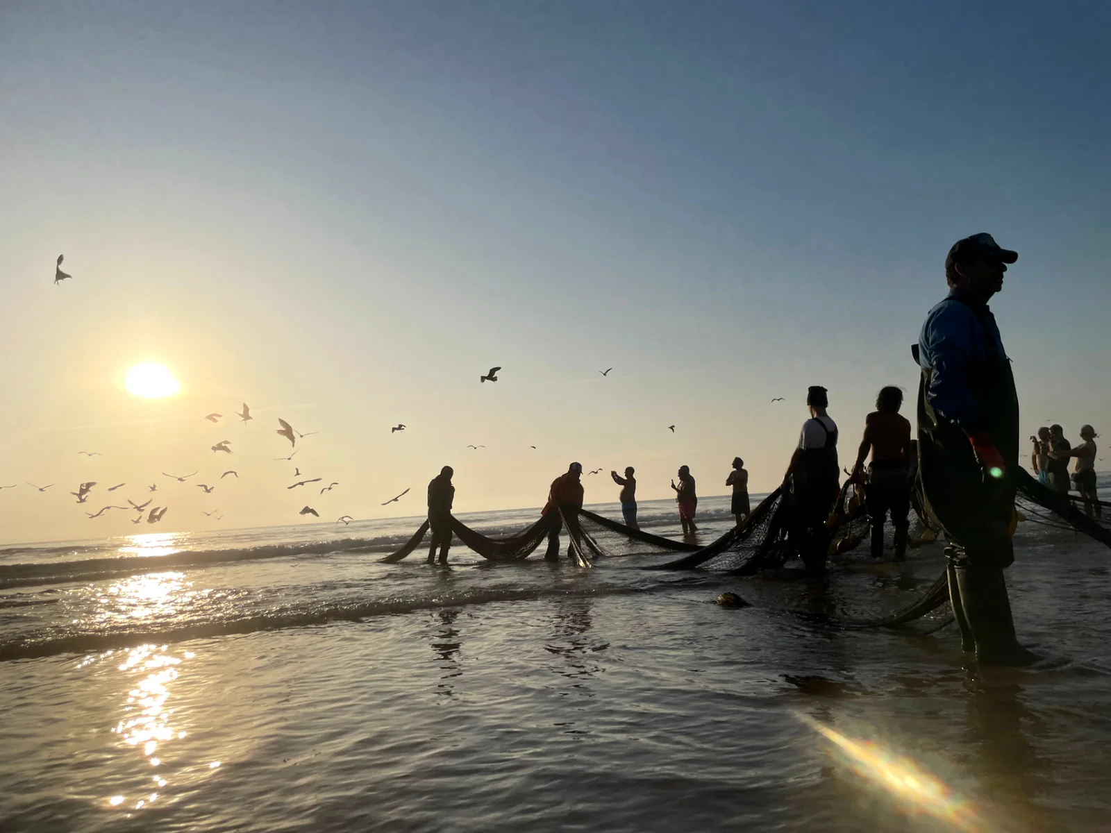 Fishers drawing nets at sunset on the Atlantic coast near Almada, Portugal